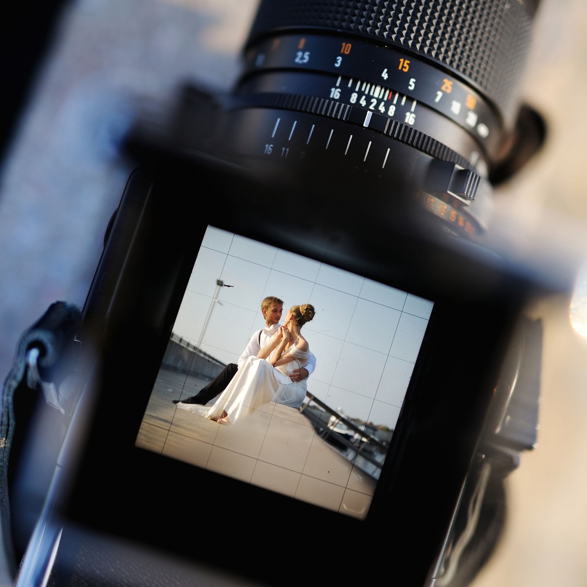 Wedding couple posing on a beach, seen through a camera viewfinder and lens display.