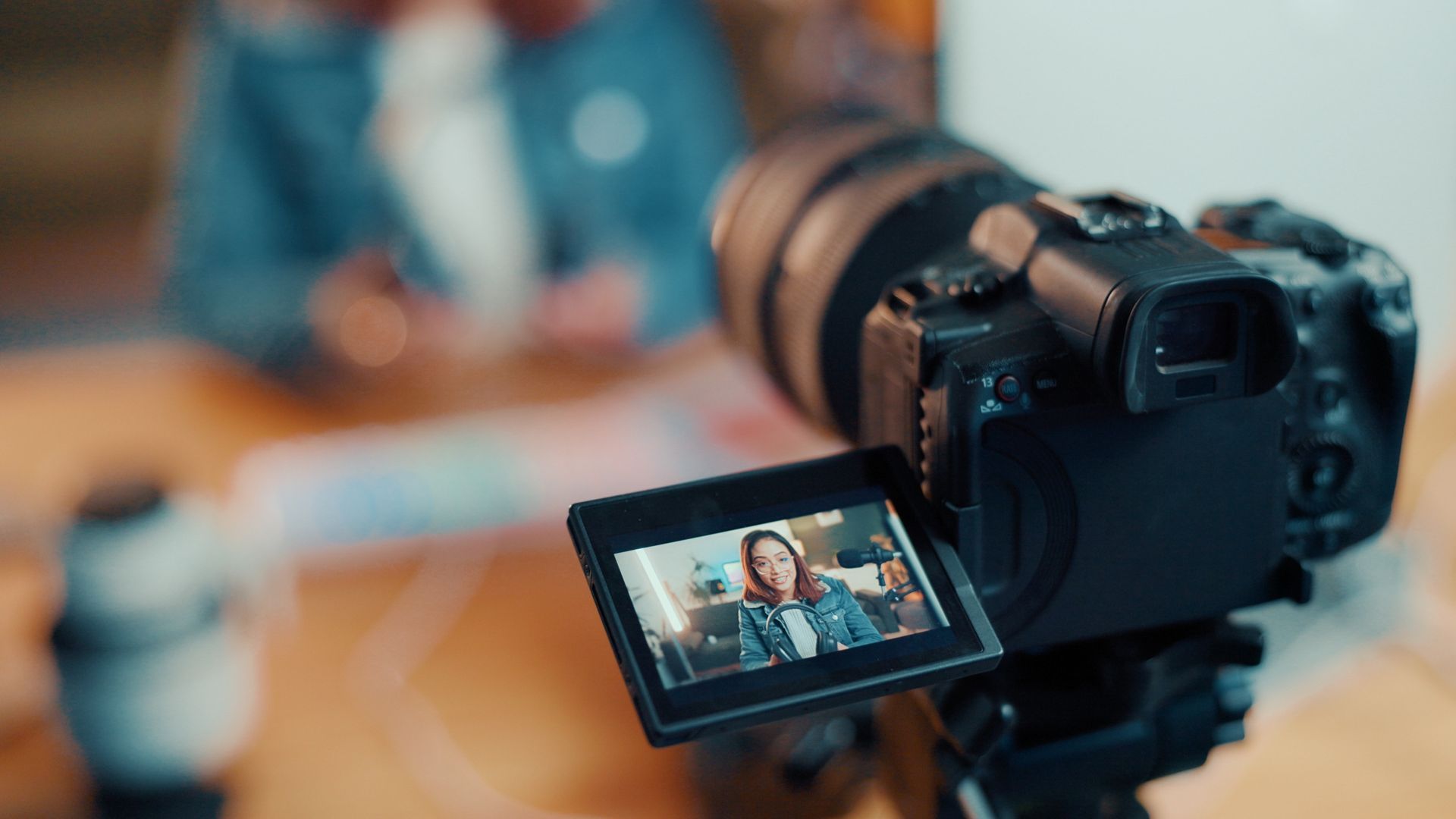 Digital camera on tripod filming a person on its flip-out screen in a blurred indoor setting