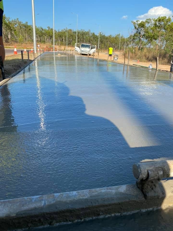Newly poured concrete surface reflecting sky and a vehicle, outdoor setting with worker in background.