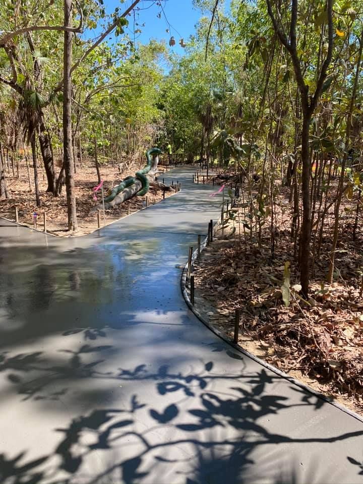 Concrete path through wooded area, with dinosaur statue in the distance.