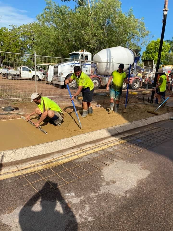 Construction workers pouring and smoothing concrete for a sidewalk on a sunny day.