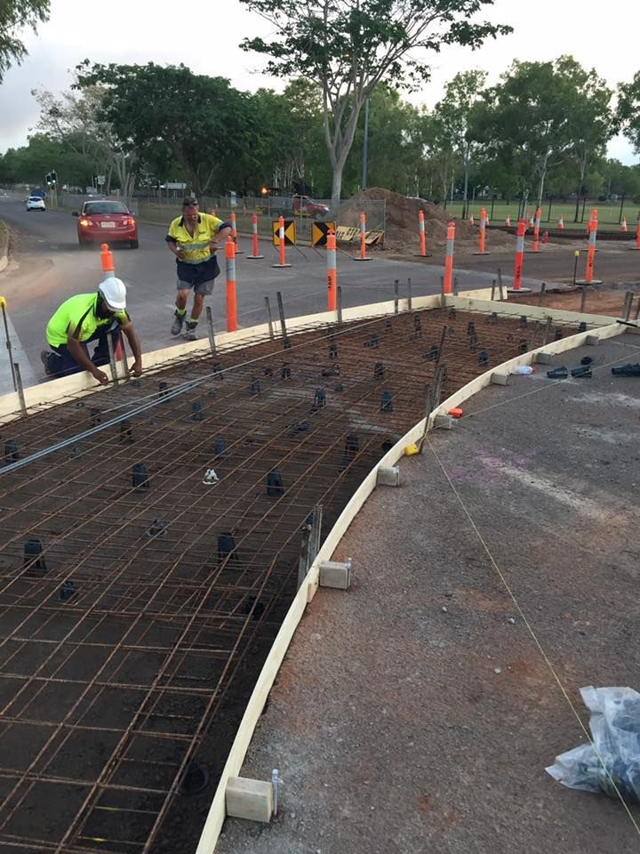 Workers constructing a curved concrete pathway on a road. Rebar and forms are in place.