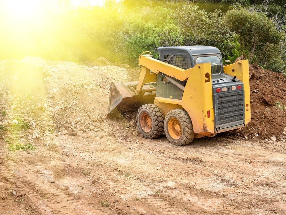 Yellow skid steer moving dirt on a construction site.