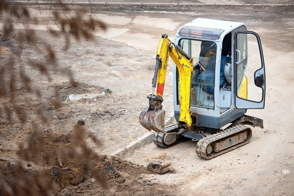 A small yellow and gray excavator digs into the ground on a construction site.