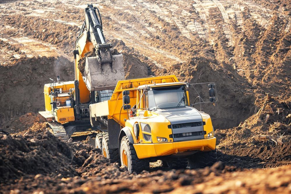 Yellow excavator loading a dump truck in a brown dirt quarry.