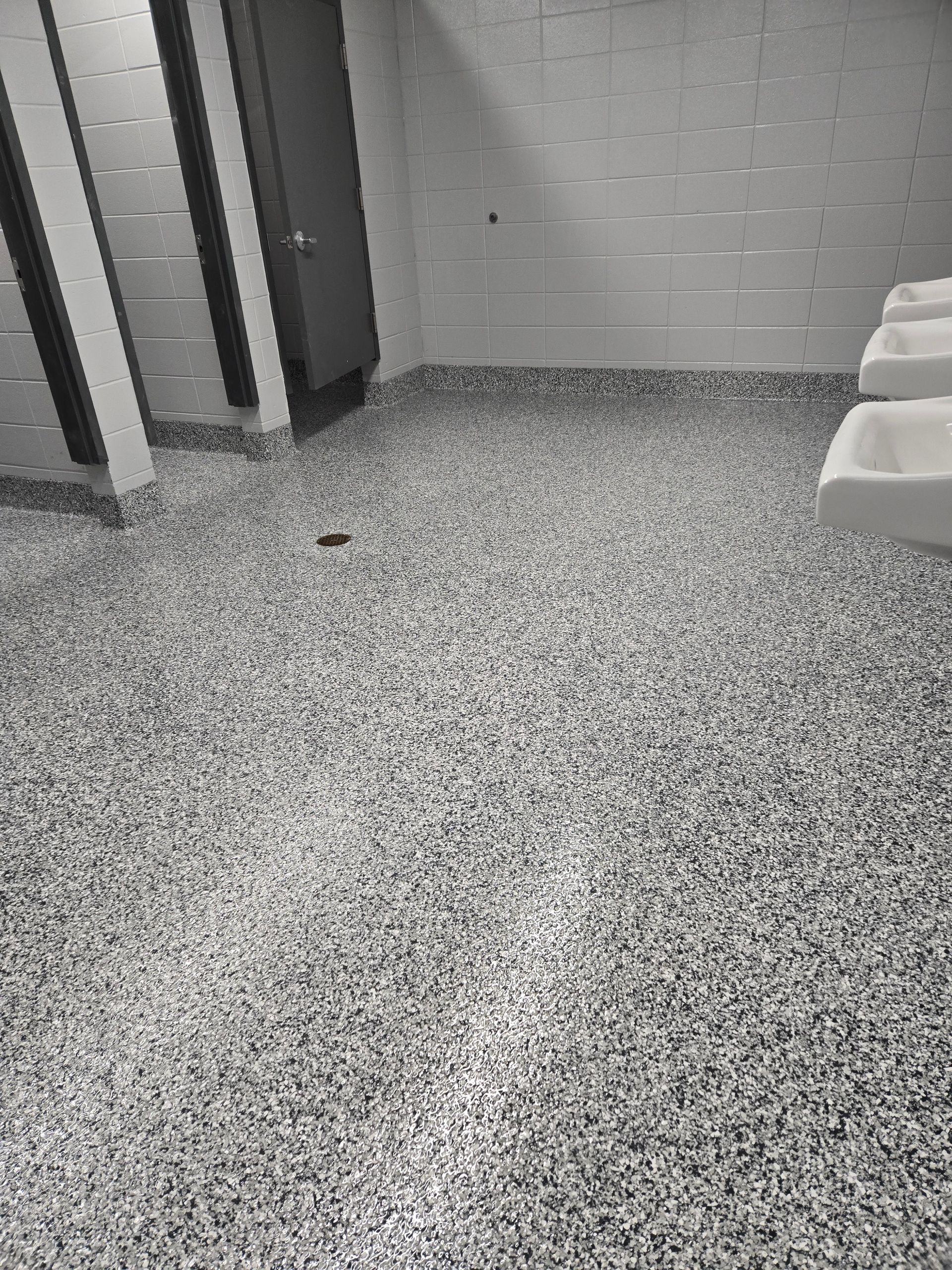 Public restroom with gray speckled epoxy flooring, white block walls, and white ceramic sinks.