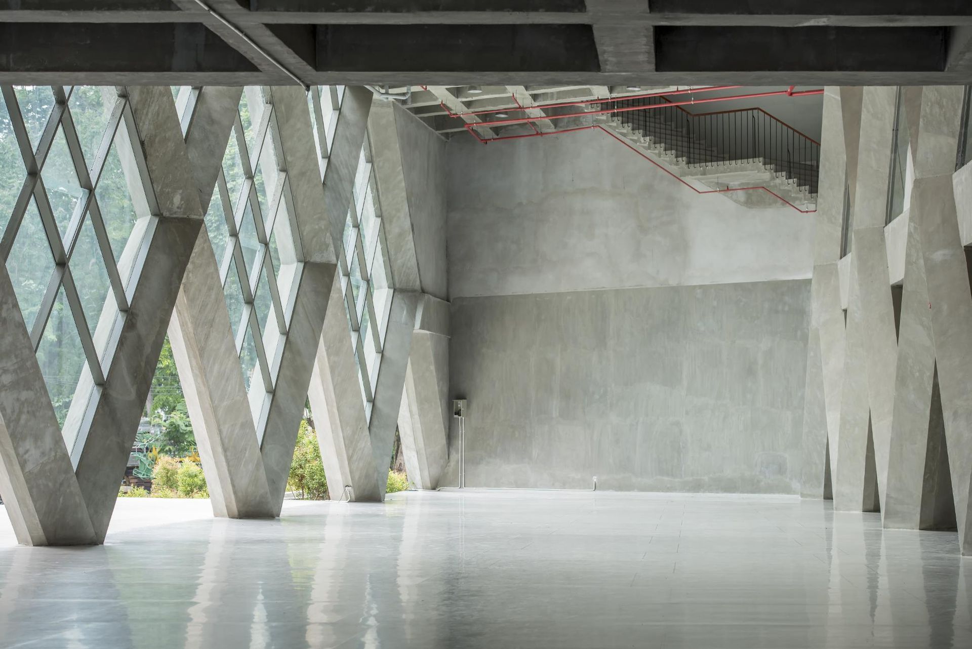 An expansive, minimalist concrete interior with geometric, zigzagging support pillars and large, diagonal glass windows.
