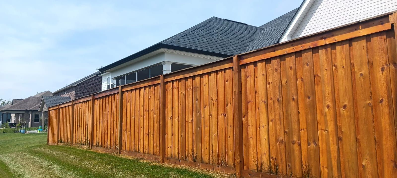 Row of tall wooden privacy fences along suburban houses beside a grassy strip