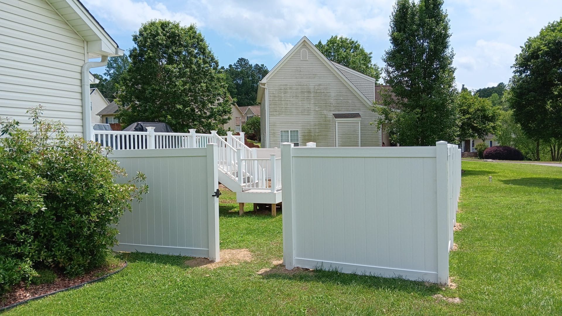 Open white fence panels in a grassy backyard with a small shed and house in the background