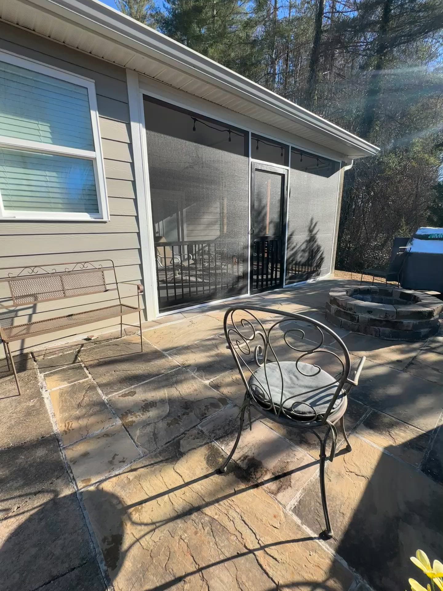 Patio beside a house with a metal chair, stone steps, and screened door in sunlight