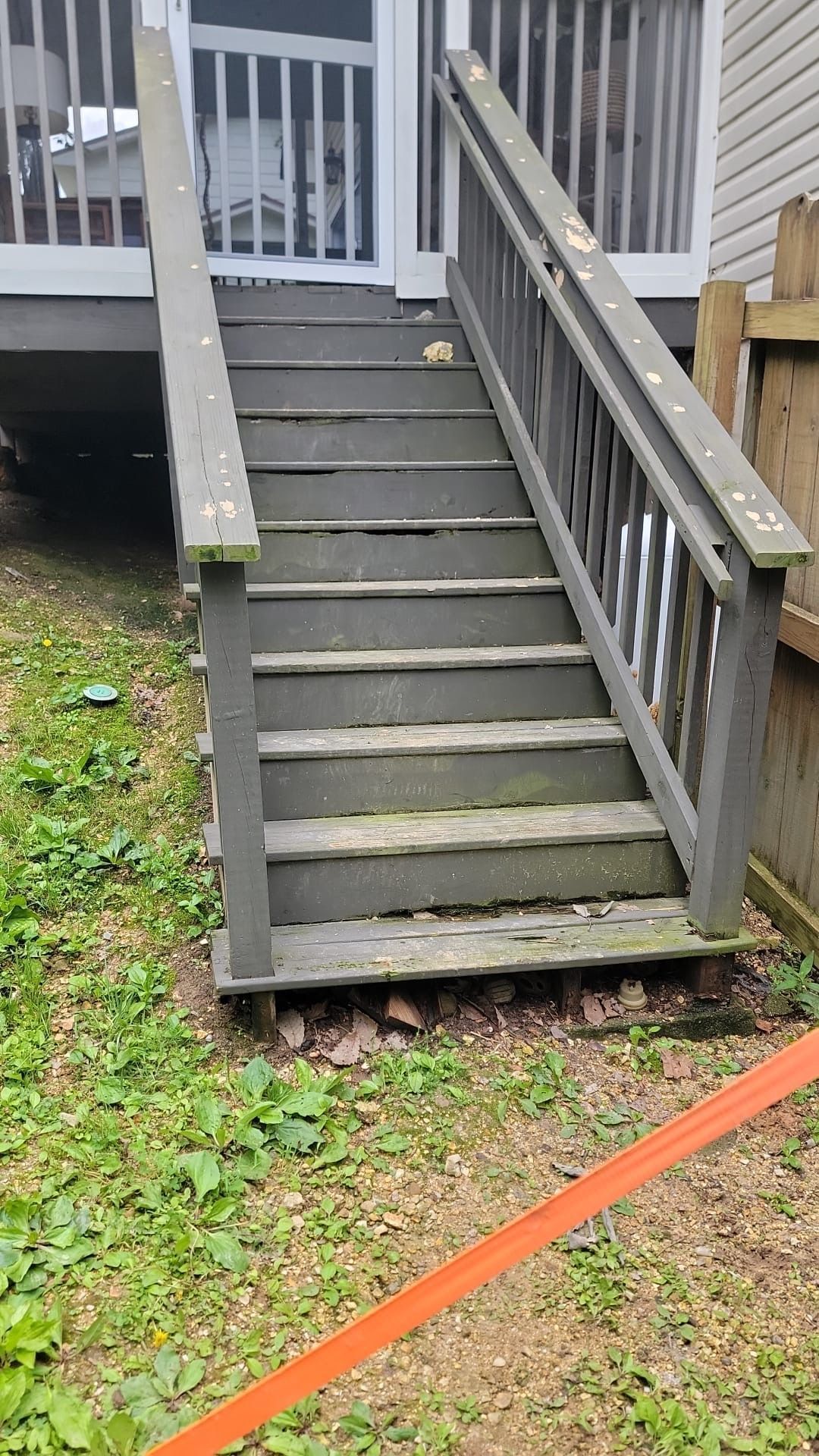 Weathered gray wooden stairs with railings leading up to a porch, with a ramp beside them.