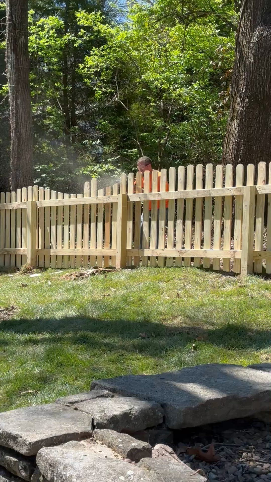 Light wooden picket fence around a grassy yard with trees and a stone step in the foreground