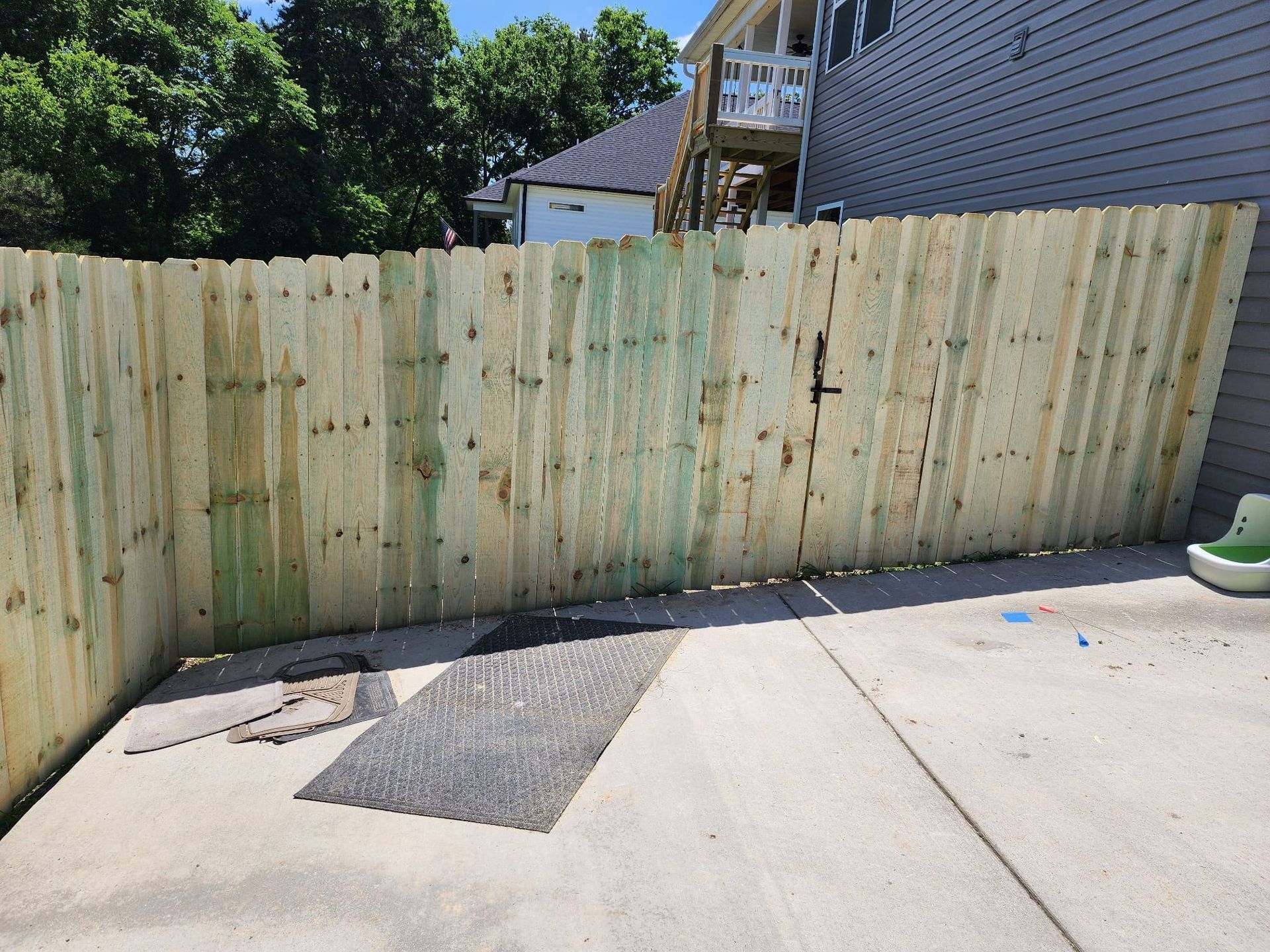 Wooden privacy fence enclosing a concrete patio, with a small mat and neighboring house visible.