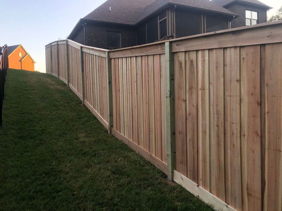 Wooden fence lines a grassy slope beside a dark house under an overcast sky.