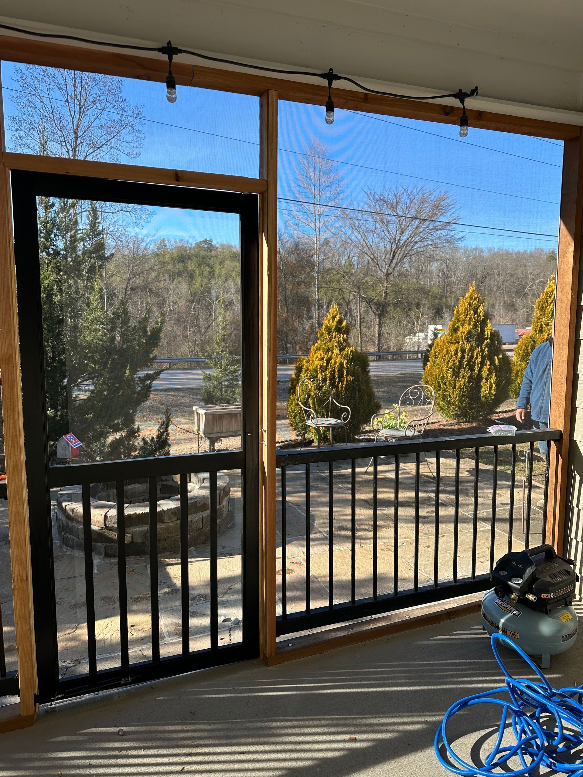 Screened porch with black railing, lake view, and coiled blue hose on the floor