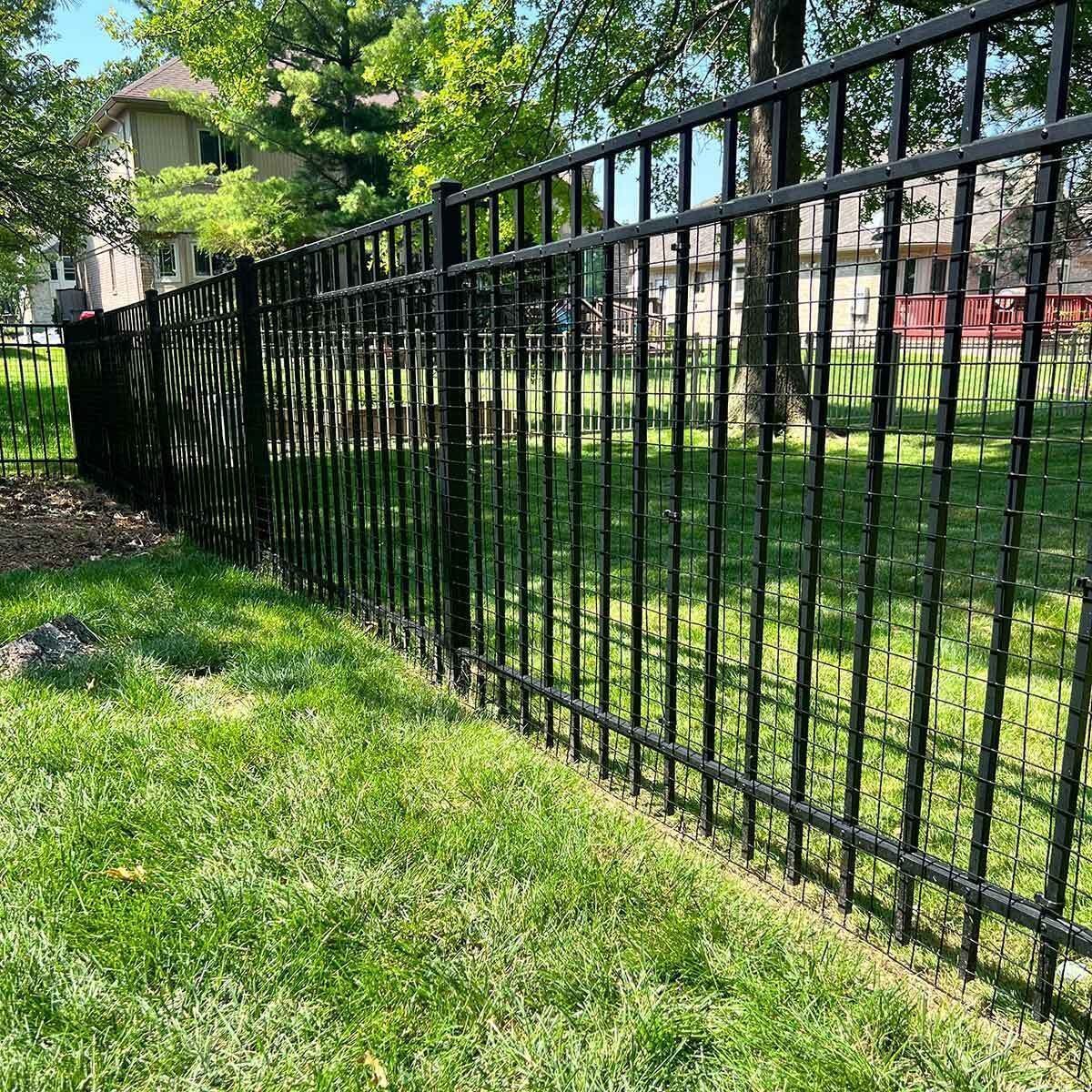 Black metal fence along a sunny grassy yard with trees and houses in the background