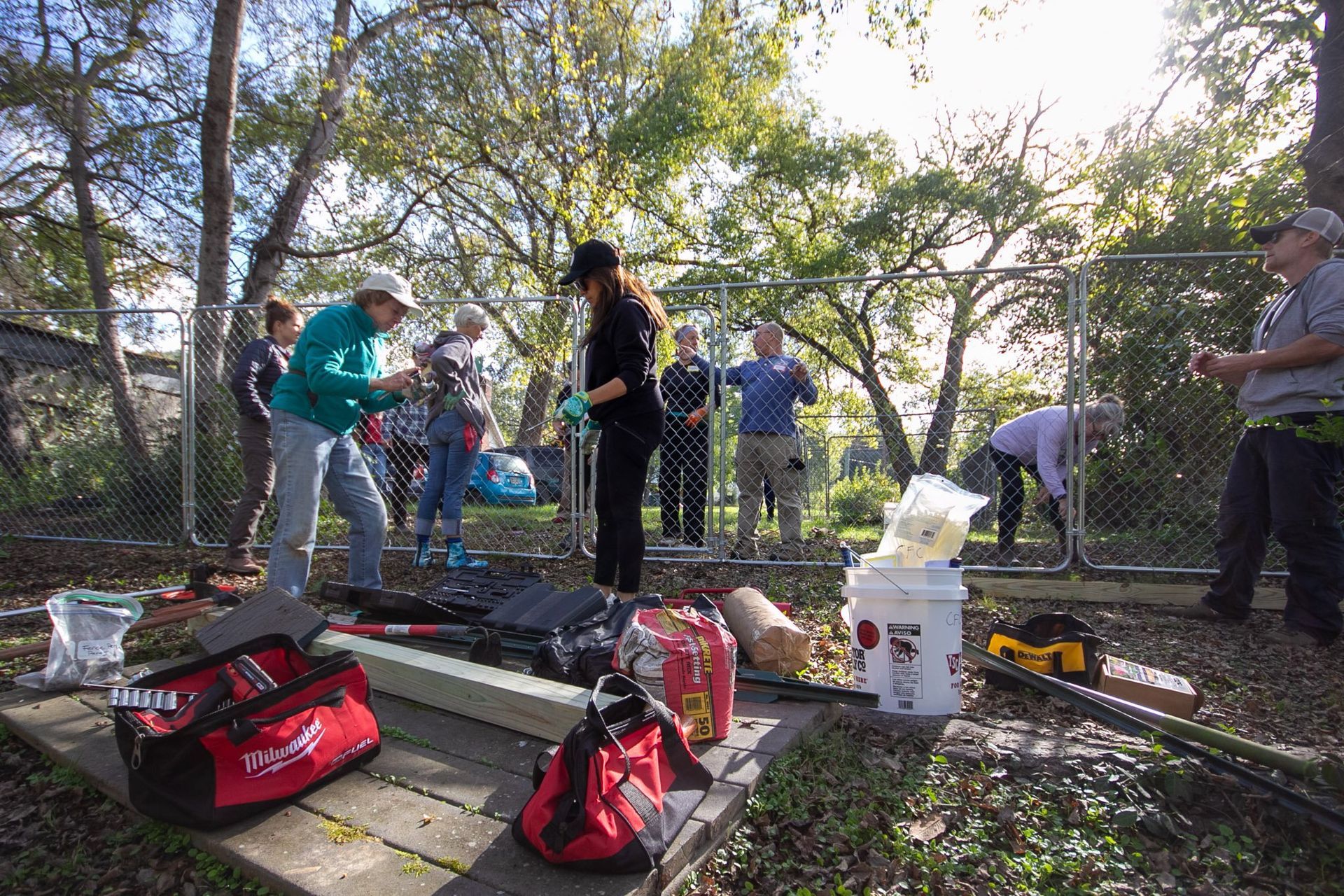 People setting up camping gear and supplies in a wooded outdoor area.