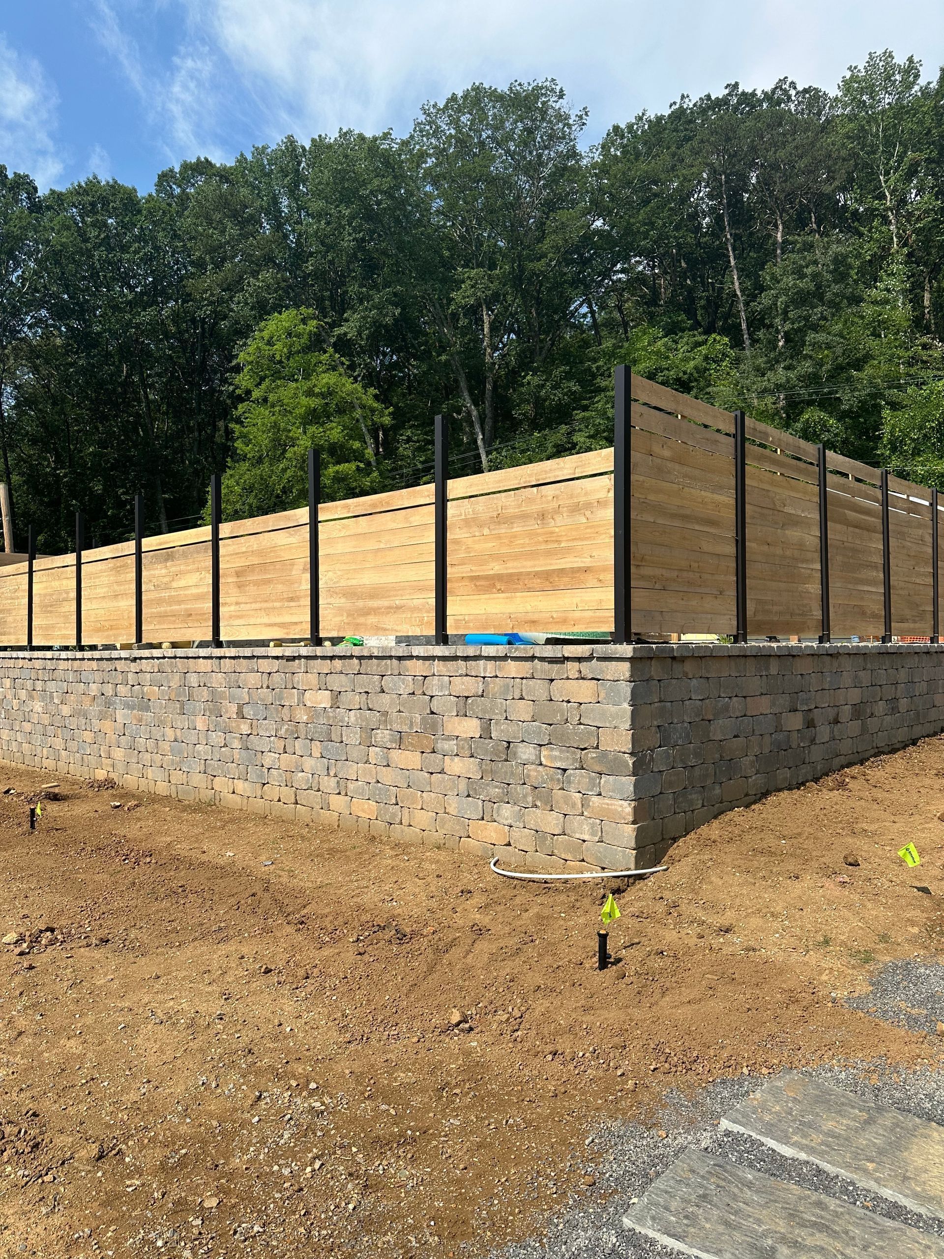 Wooden retaining wall and fencing atop a stone foundation on a dirt slope beside trees and sky