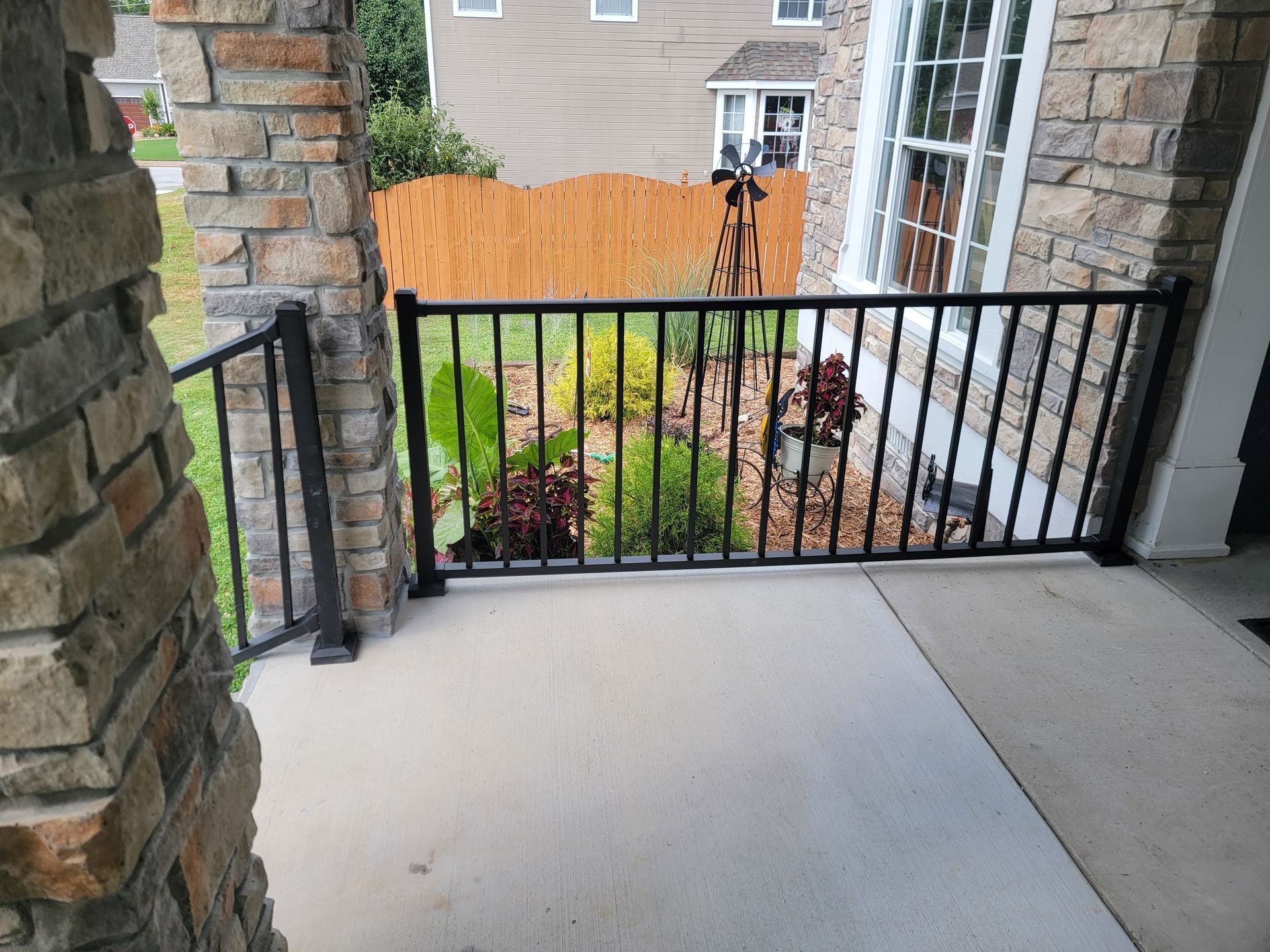 Porch patio with black railing overlooking a landscaped courtyard and brick apartment buildings