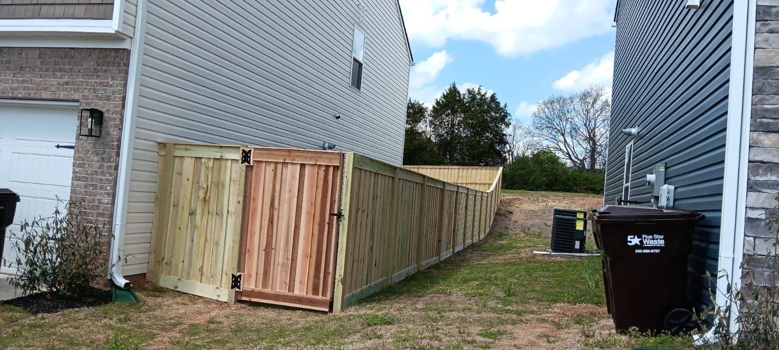 Wooden privacy fence between two houses beside a grassy side yard and trash bin