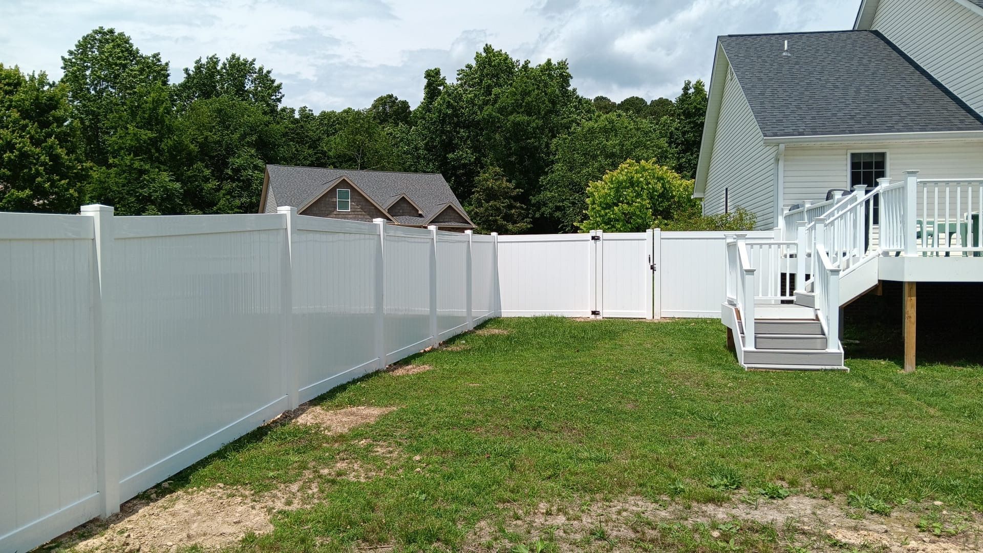 Backyard with white vinyl fence, grass lawn, and a house deck with stairs on the right.