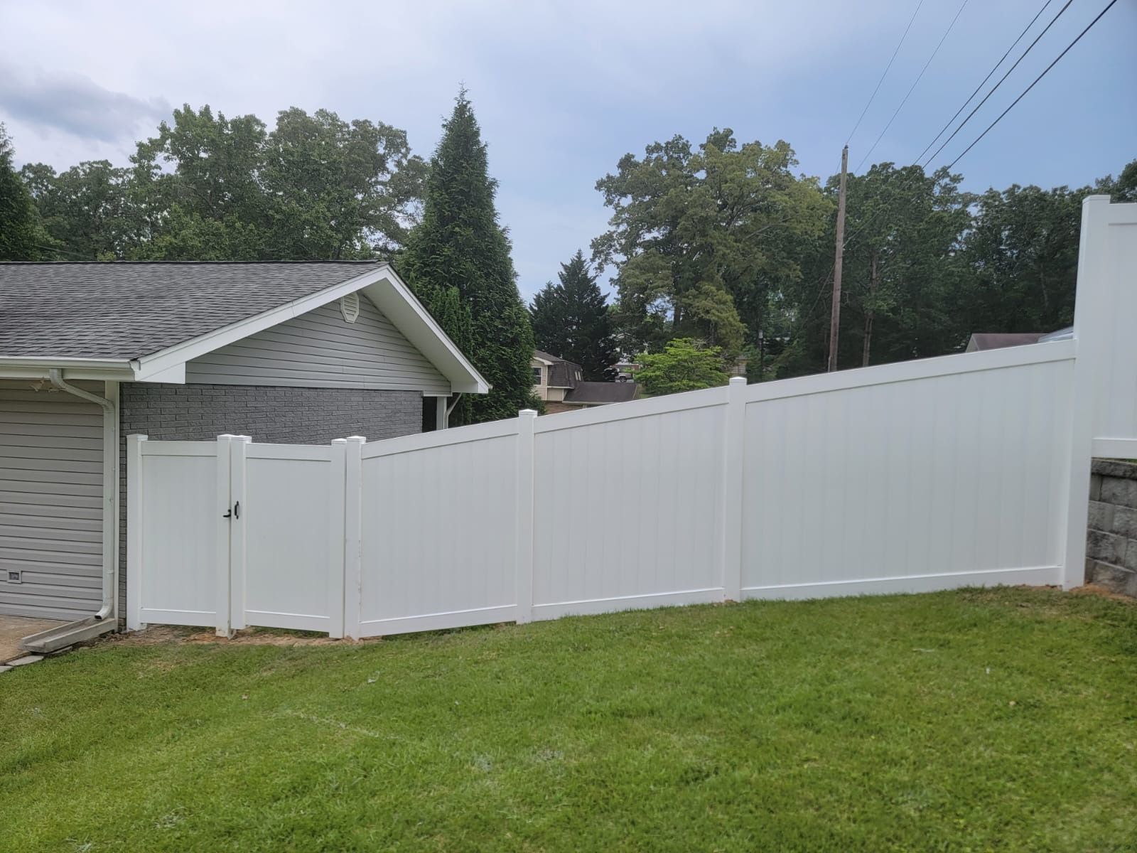 White vinyl privacy fence along a grassy yard beside a house and garage under a cloudy sky