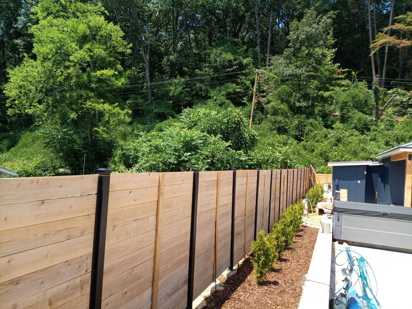 Wooden privacy fence beside a landscaped yard with small shrubs and trees in the background