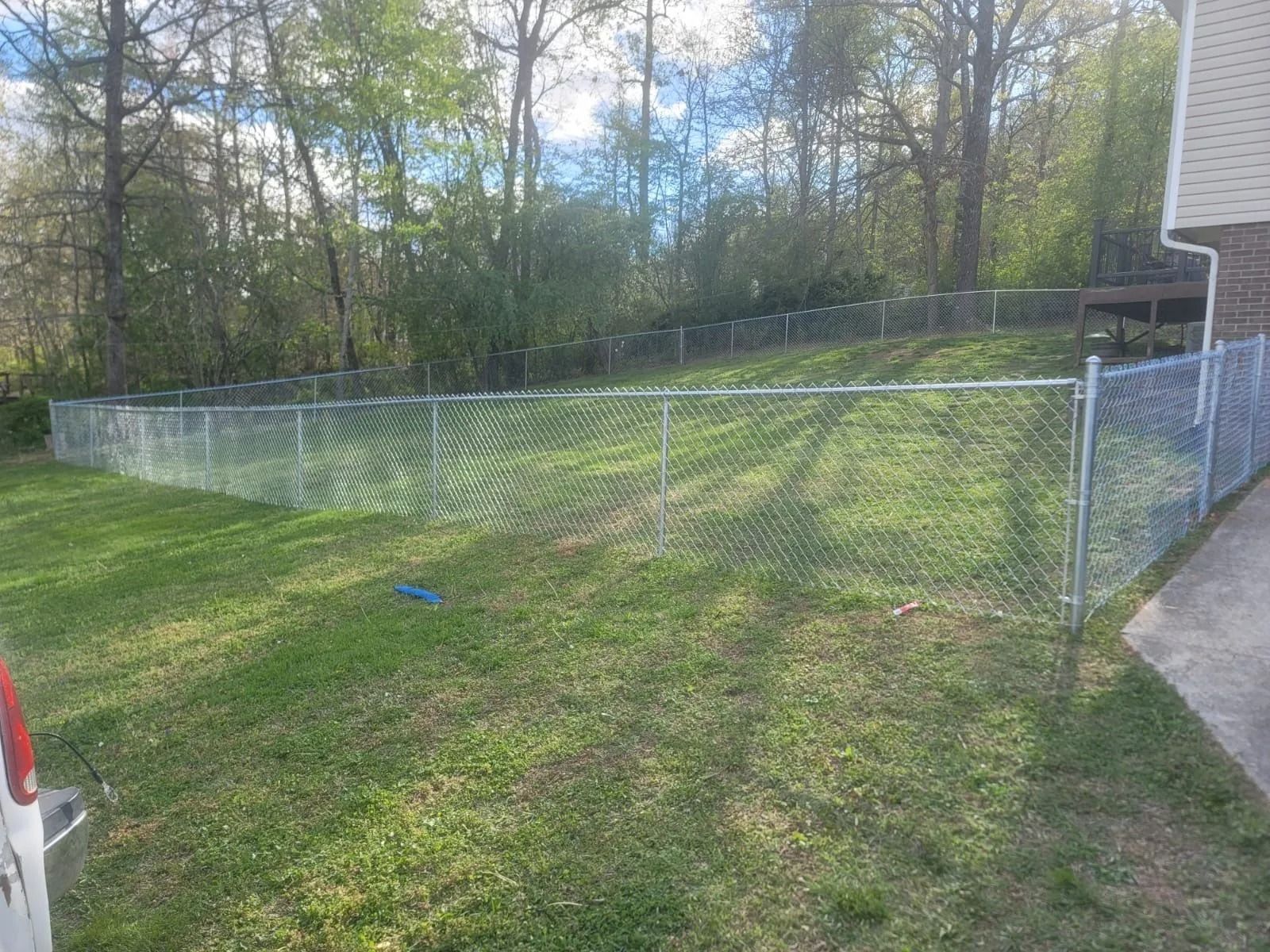 Chain-link fence enclosing a grassy backyard beside a house, with trees in the background.