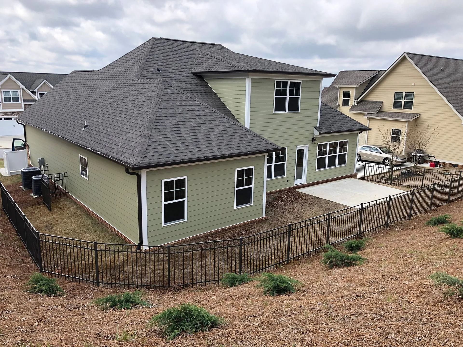 Suburban house with dark gray roof, green siding, fenced yard, and a small patio area