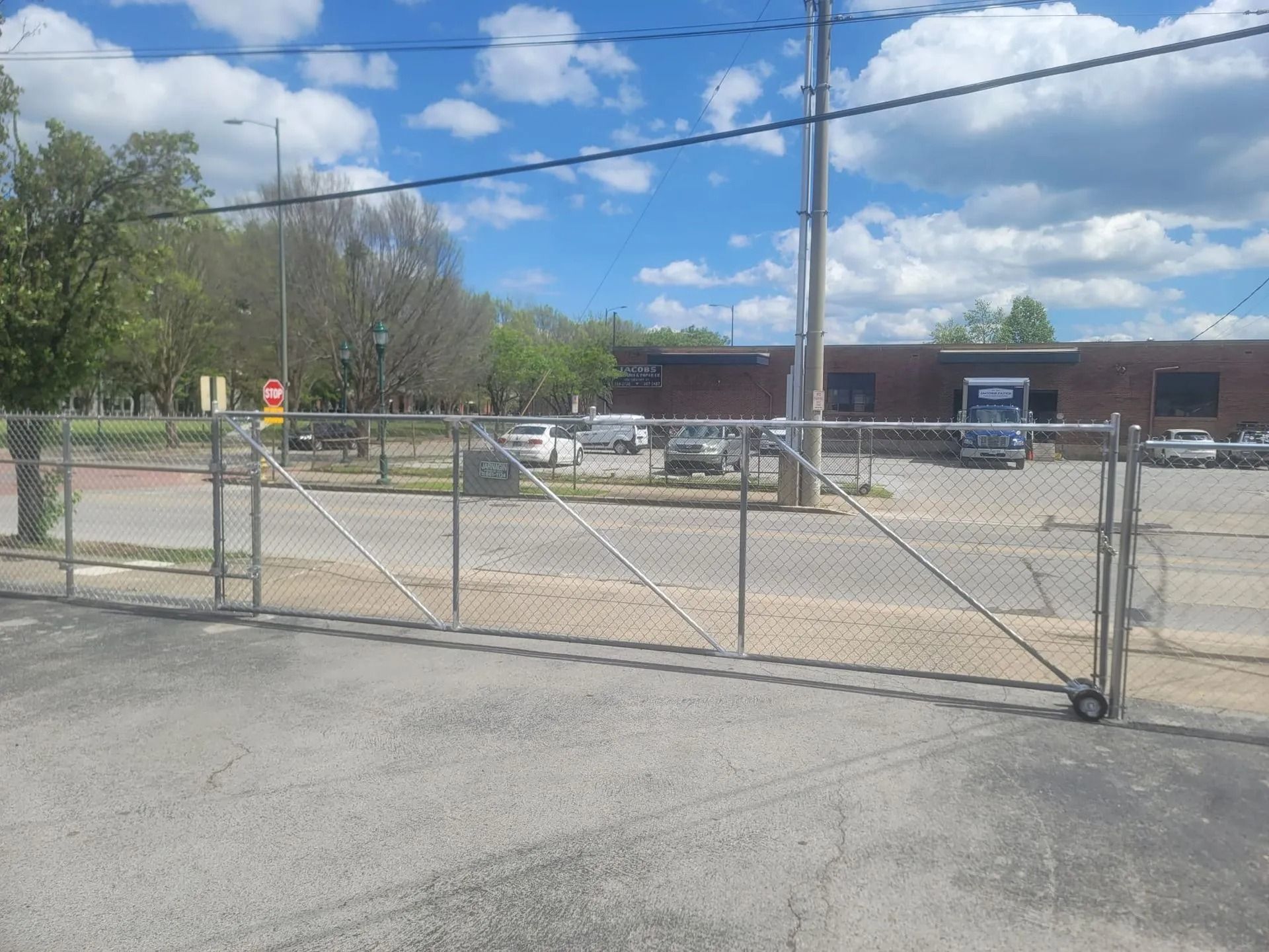 Chain-link gate at an empty parking lot beside a brick building under a partly cloudy sky