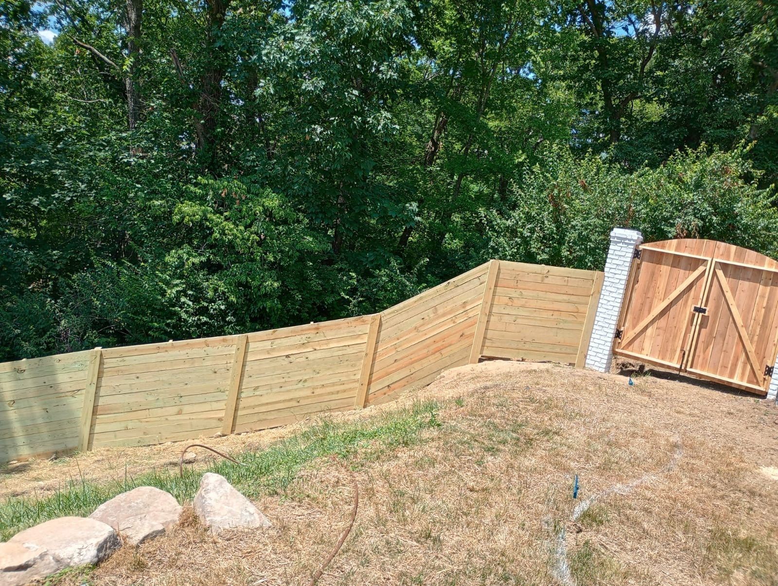 Wooden fence and gate on a grassy slope beside a wooded area