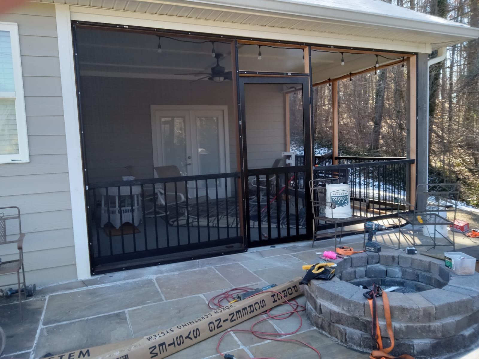 Covered patio with black railing and screen door beside a house, with stone steps under construction