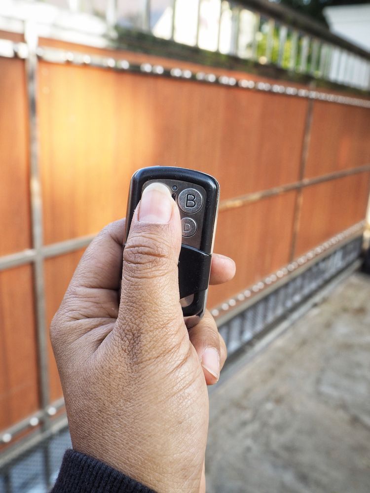 Hand holding a car key fob in front of a wooden gate outdoors