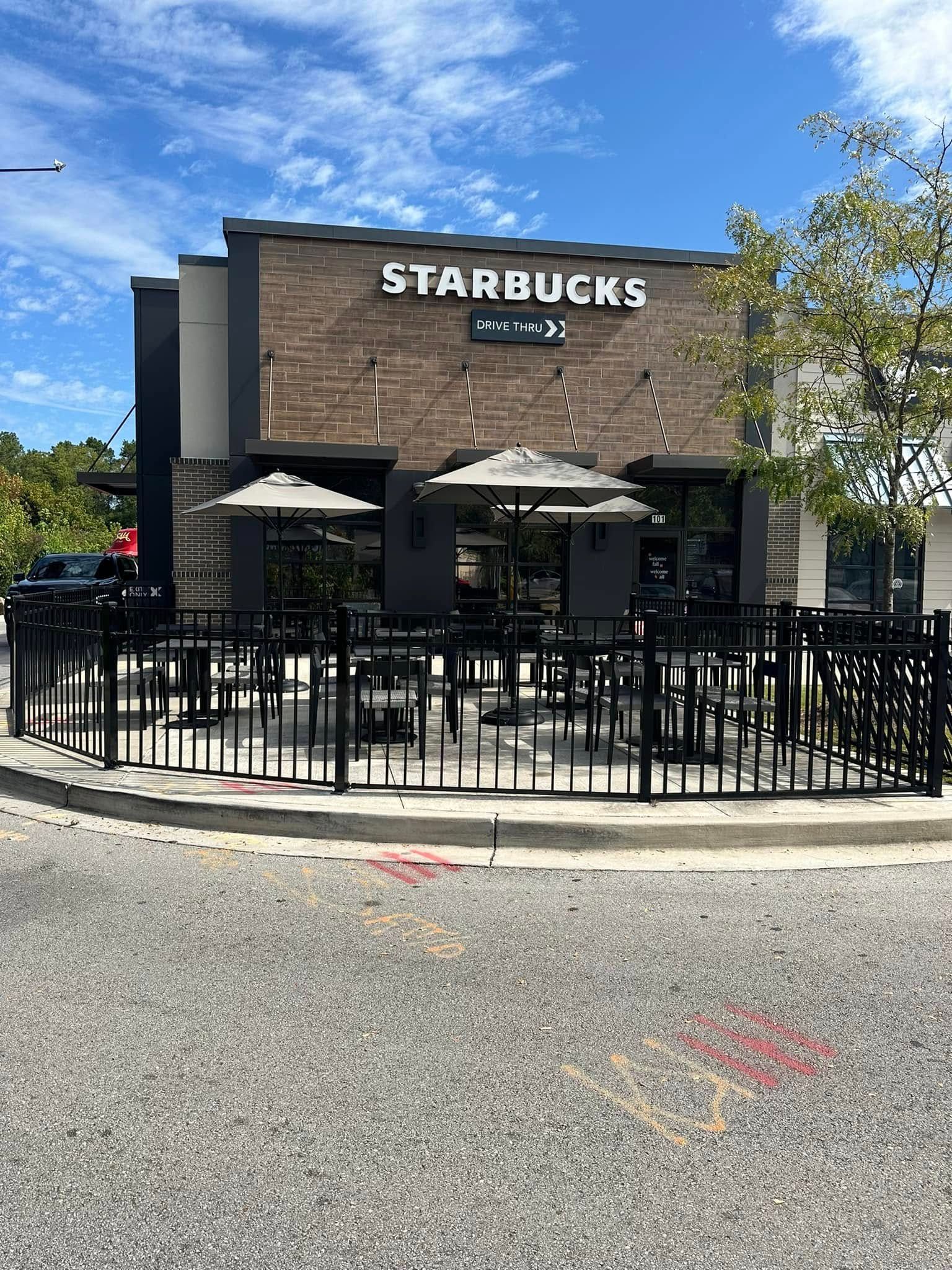 Starbucks storefront with outdoor seating and black metal fencing under a blue sky
