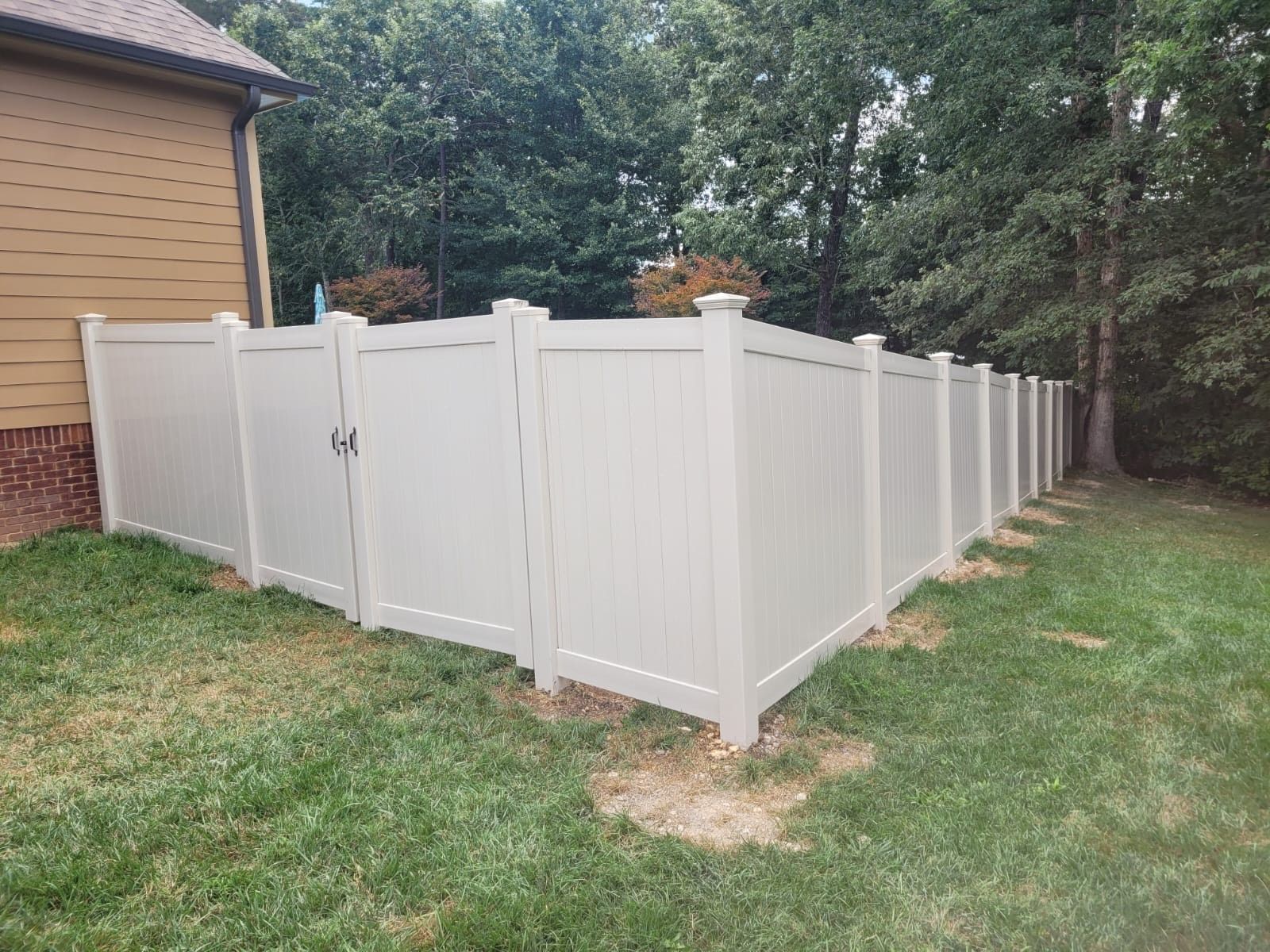 Beige privacy fence enclosing a backyard beside a house and trees