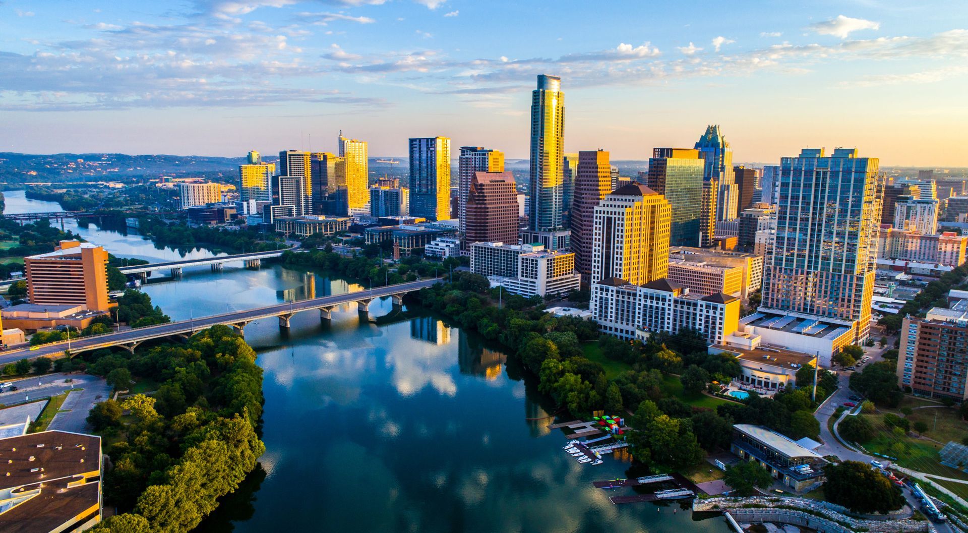 Aerial view of the Austin, Texas skyline, reflecting city skyscrapers in the Colorado River at sunset.