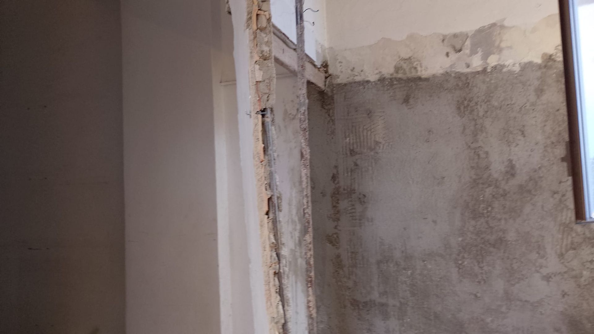 Parete interna parzialmente ristrutturata, con intonaco a vista e una porta sulla destra