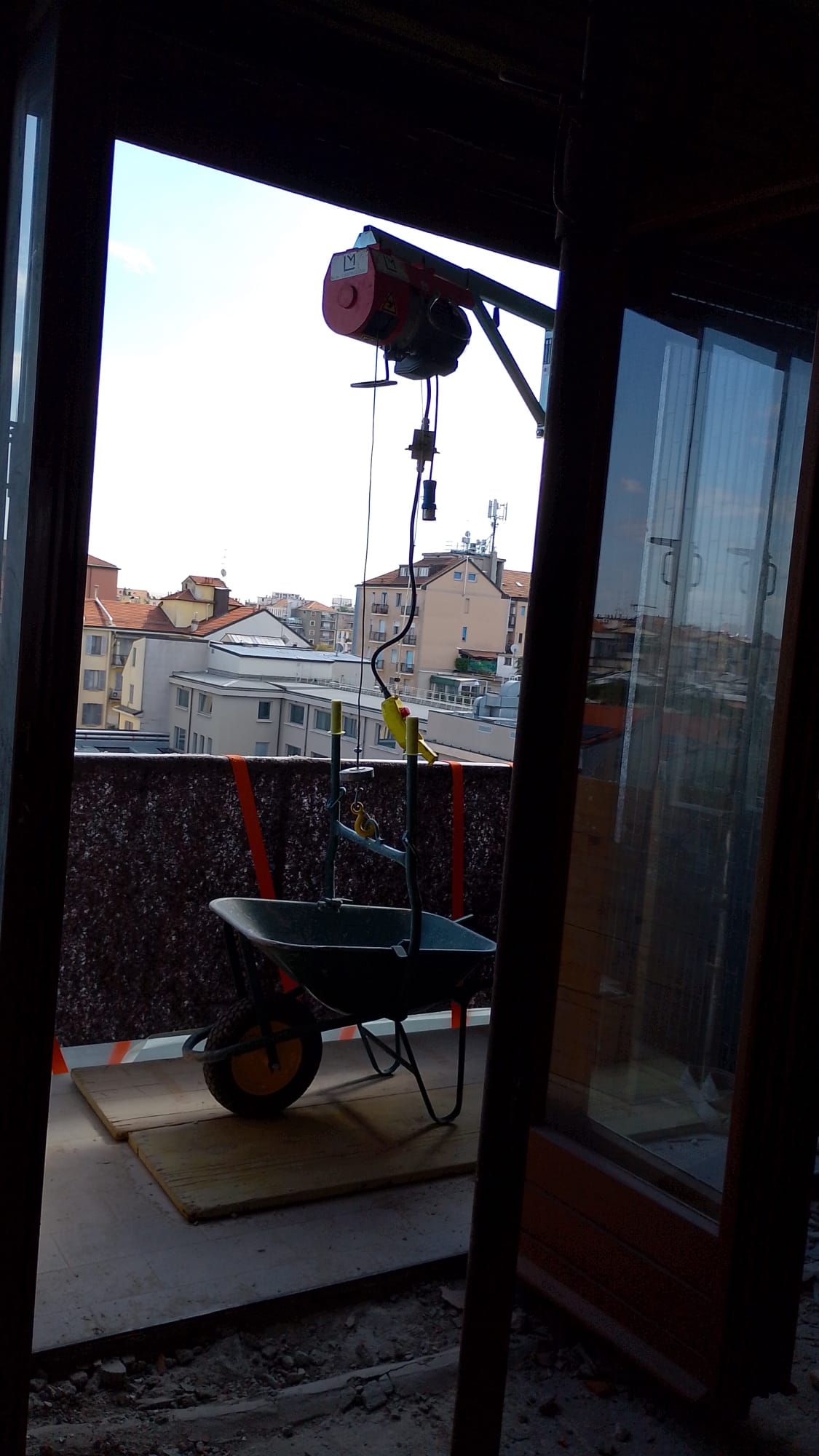 Carriola su un balcone accanto a un paranco sospeso, con vista sui tetti e sulle case al crepuscolo.