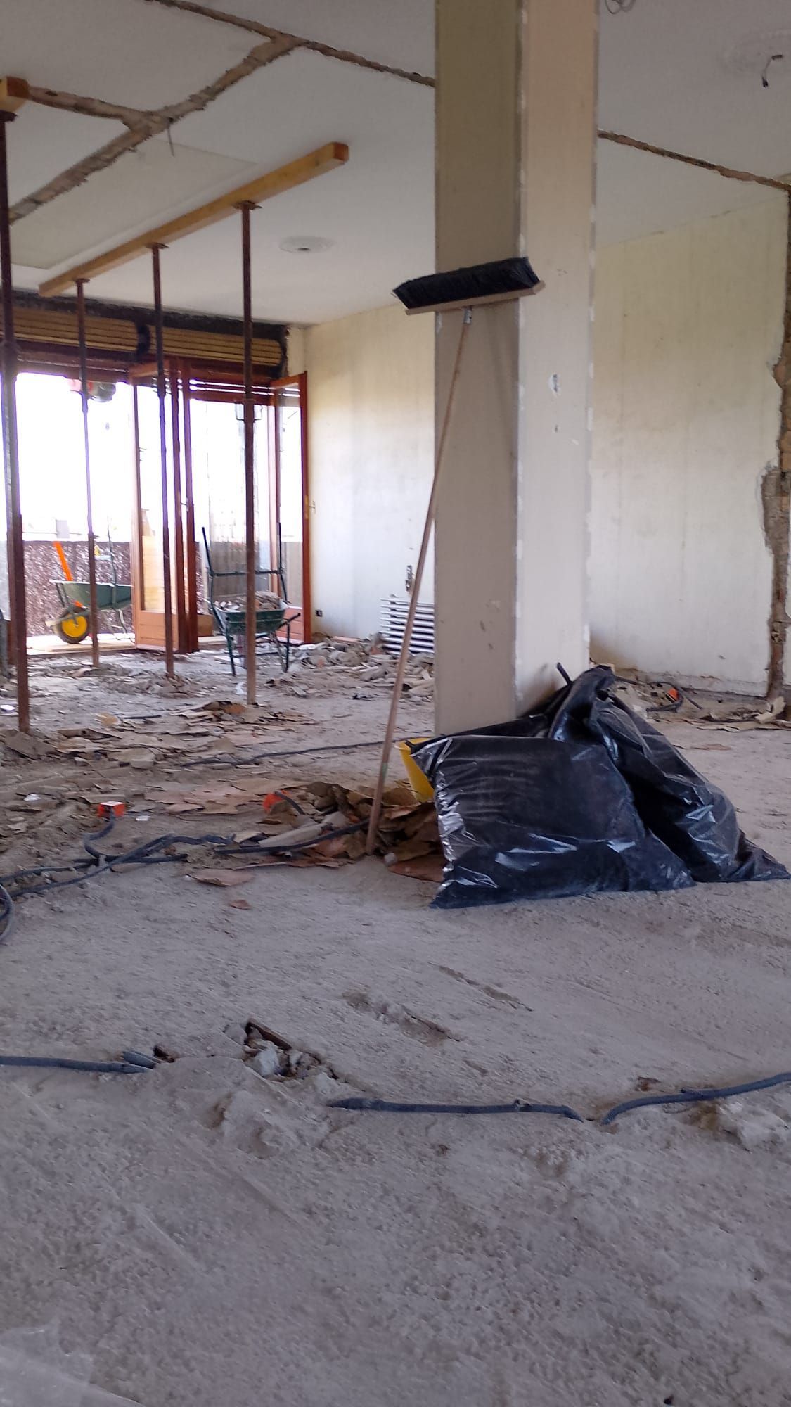 Interno di un edificio demolito, con travi a vista, macerie sul pavimento e un sacco della spazzatura nero vicino a una colonna