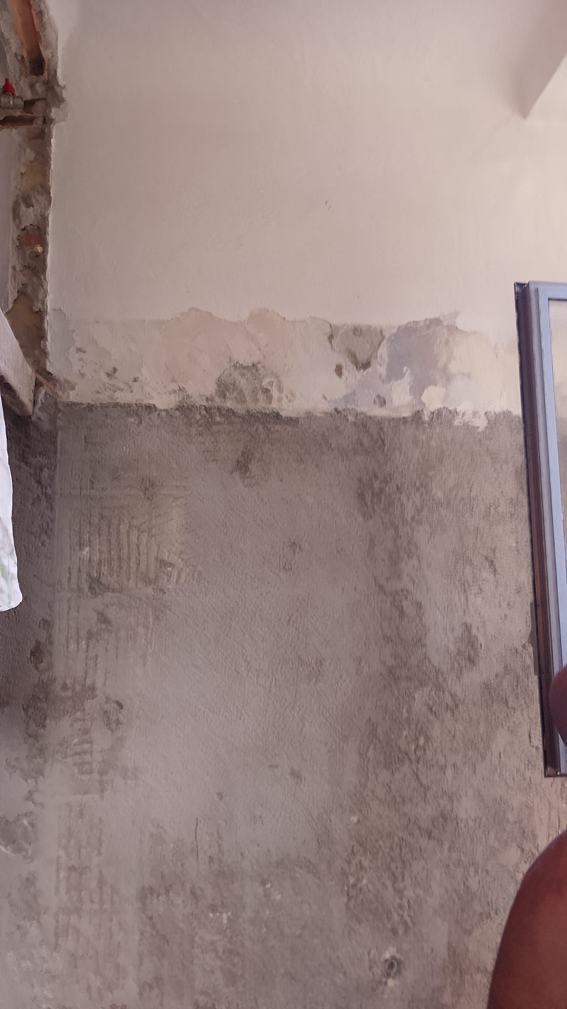 Parete scrostata e danneggiata dall’acqua, con intonaco grigio a vista, in una stanza interna