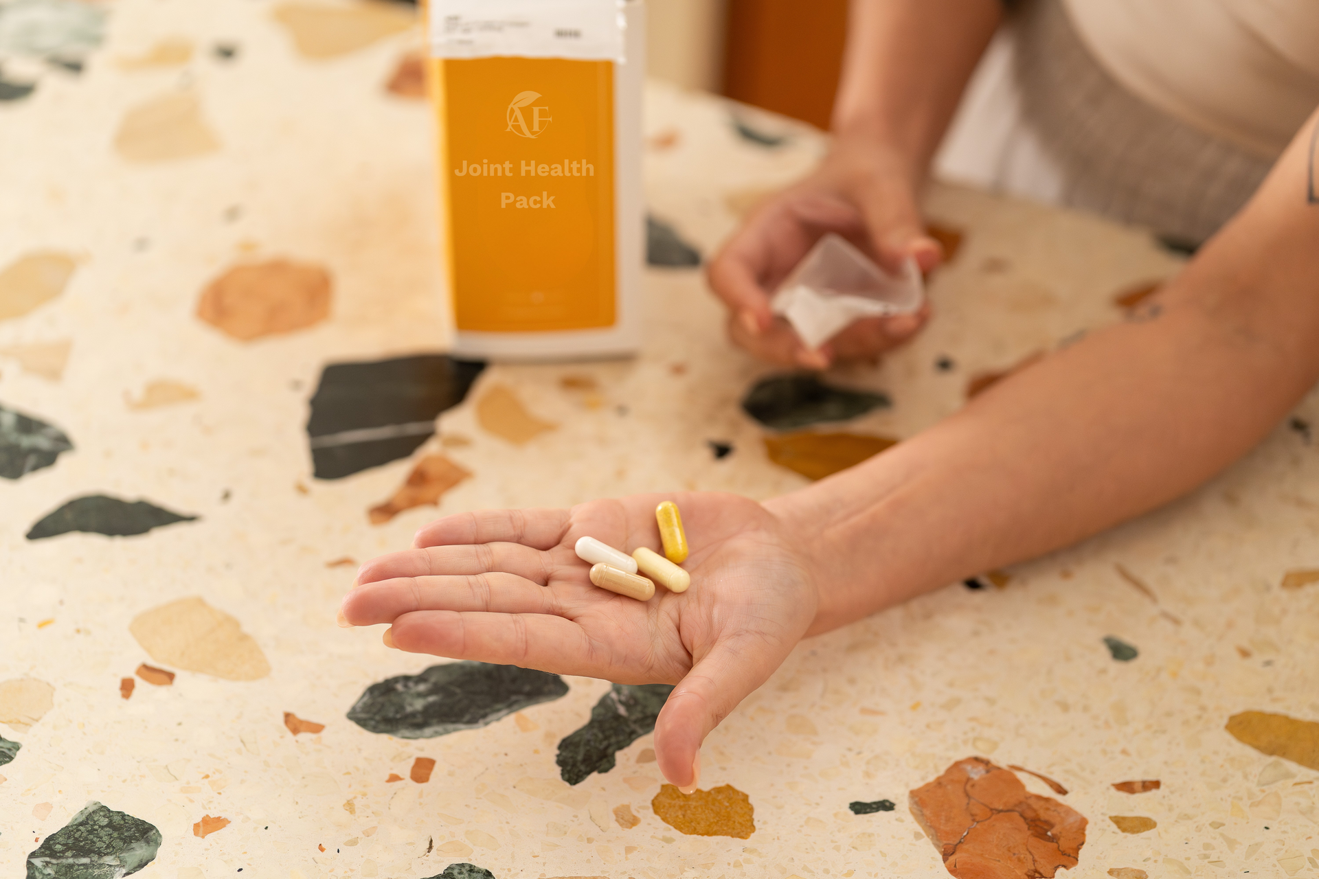 Person holding pills, bottle of supplements, pouring from a small container on a terrazzo table.