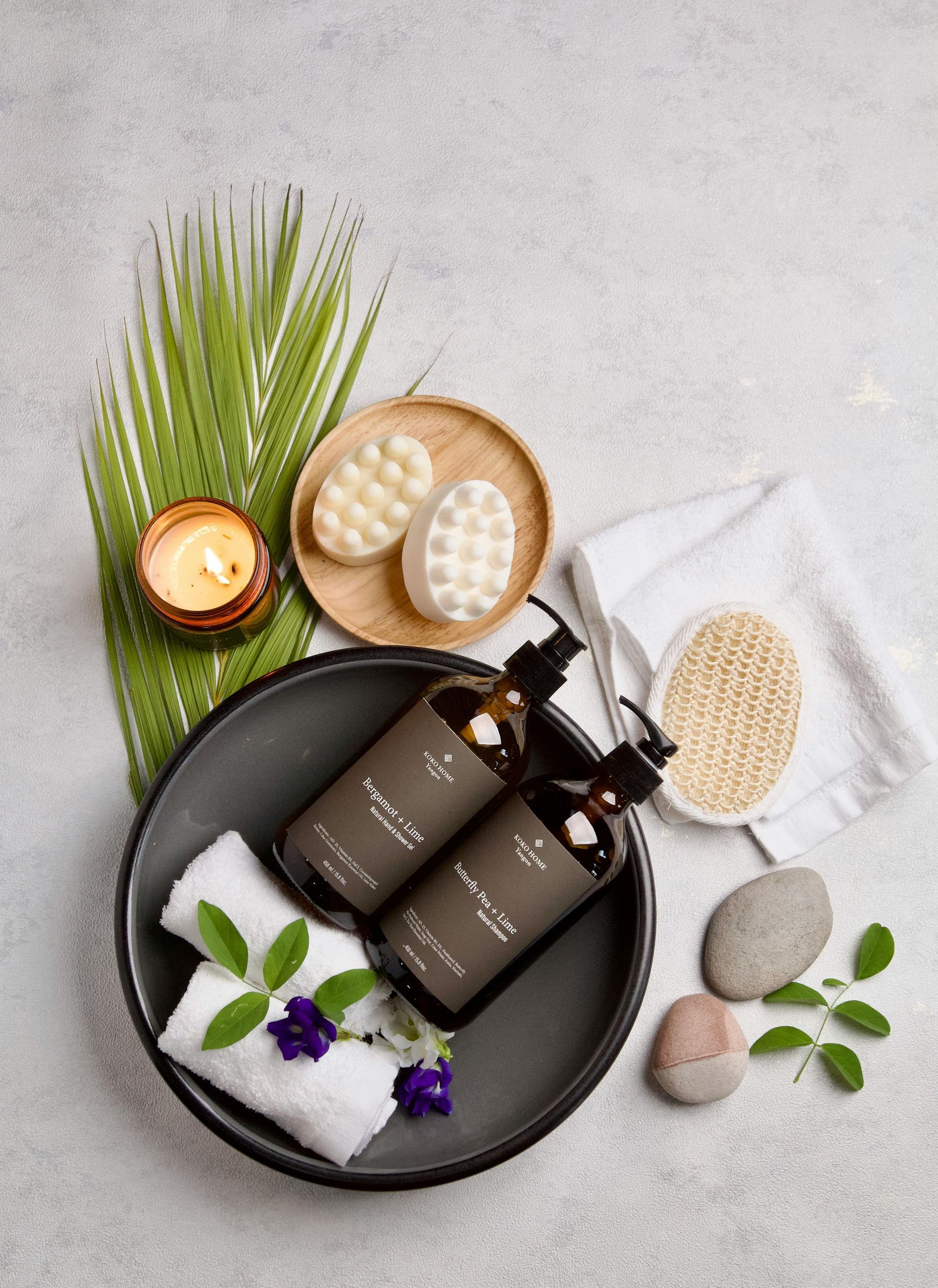 A bowl filled with bottles of soap , towels , candles , and rocks.