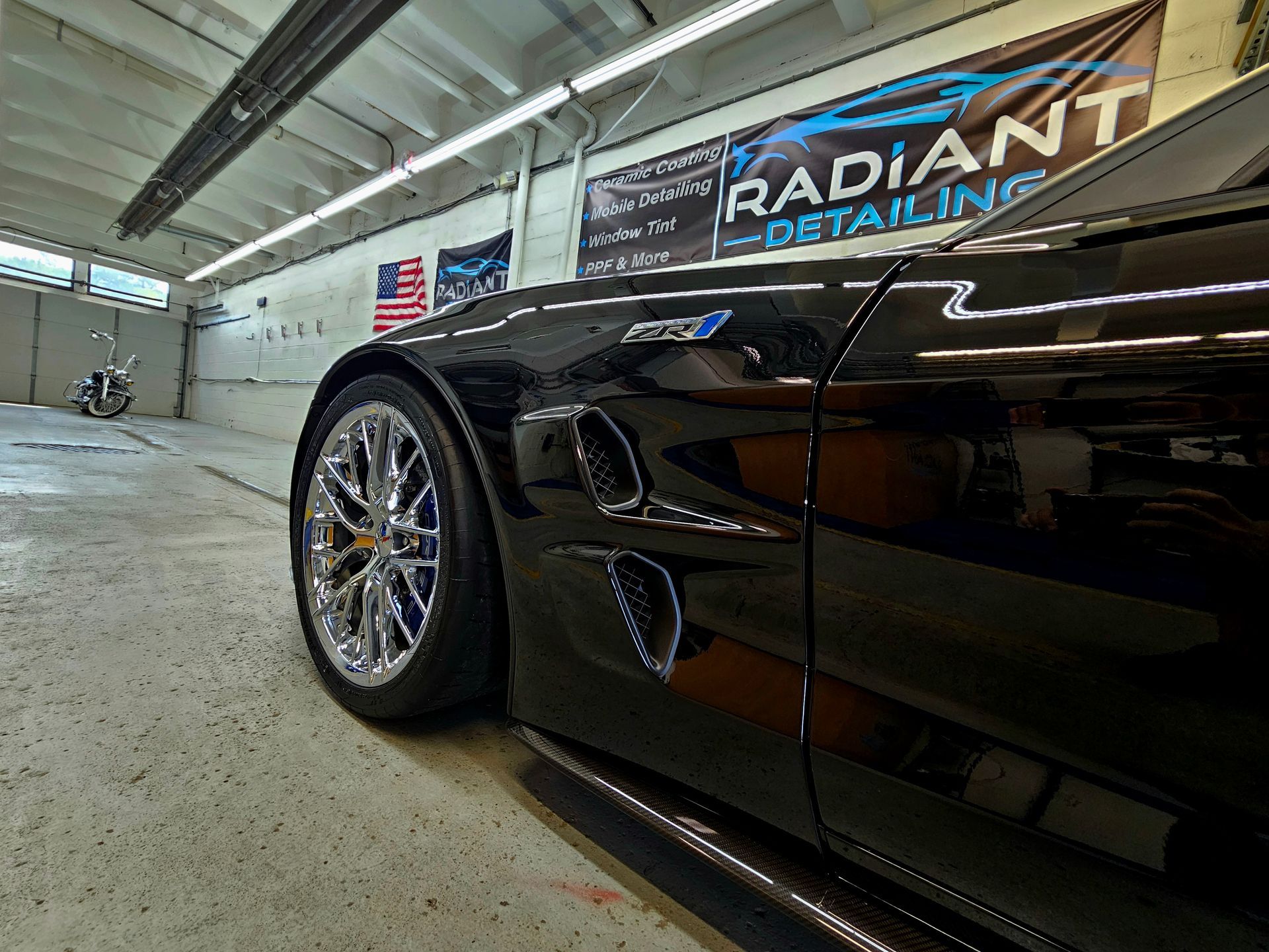 A black car is parked in a garage next to a sign that says radiant detailing.