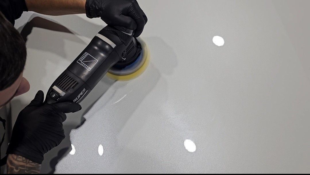 A man is polishing a white car with a machine.