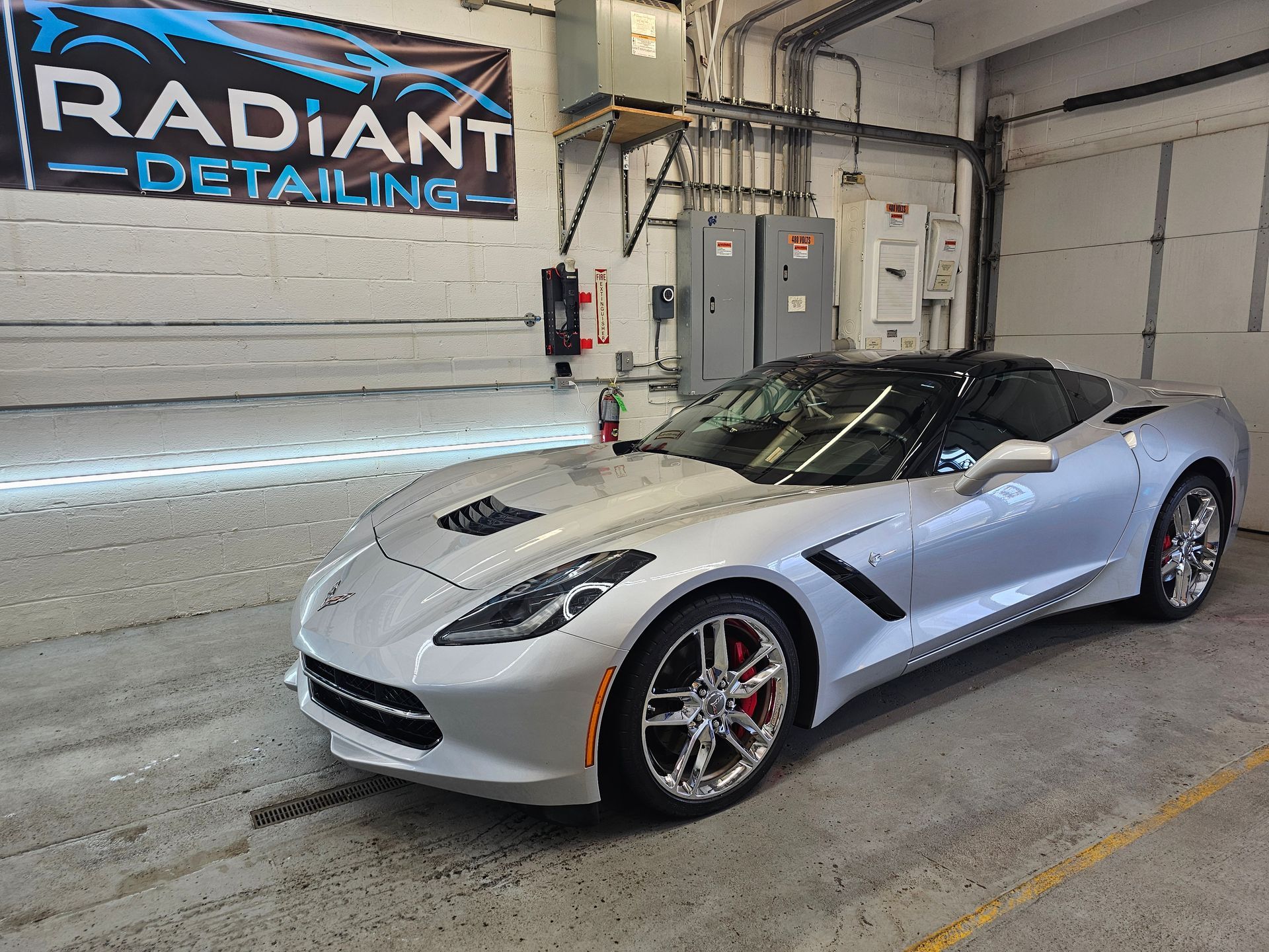 A silver sports car is parked in front of a sign that says radiant detailing.