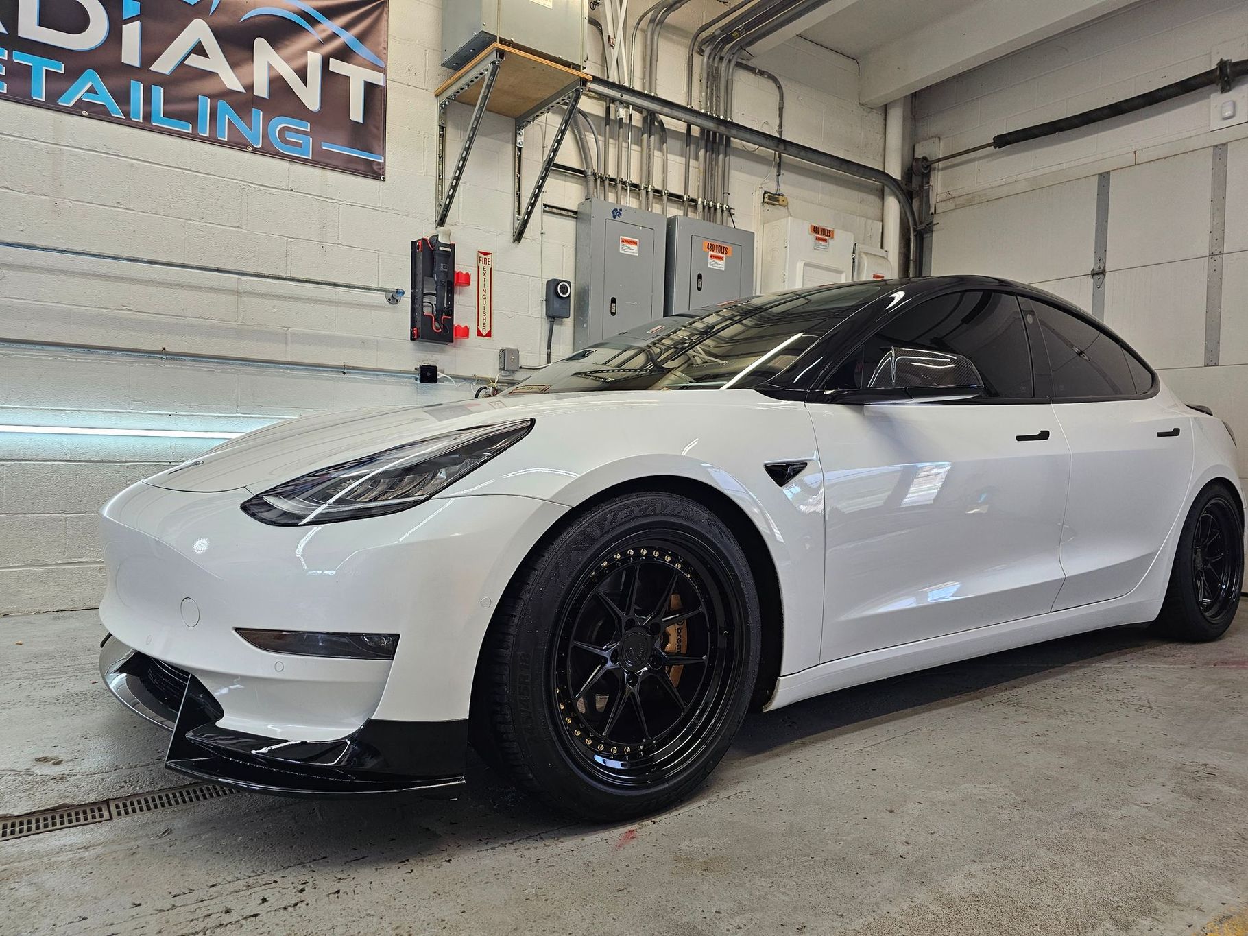A white tesla model 3 is parked in a garage.