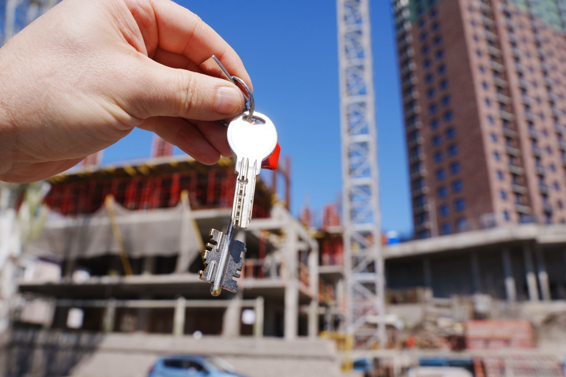 Hand holding house keys in front of building under construction and crane.