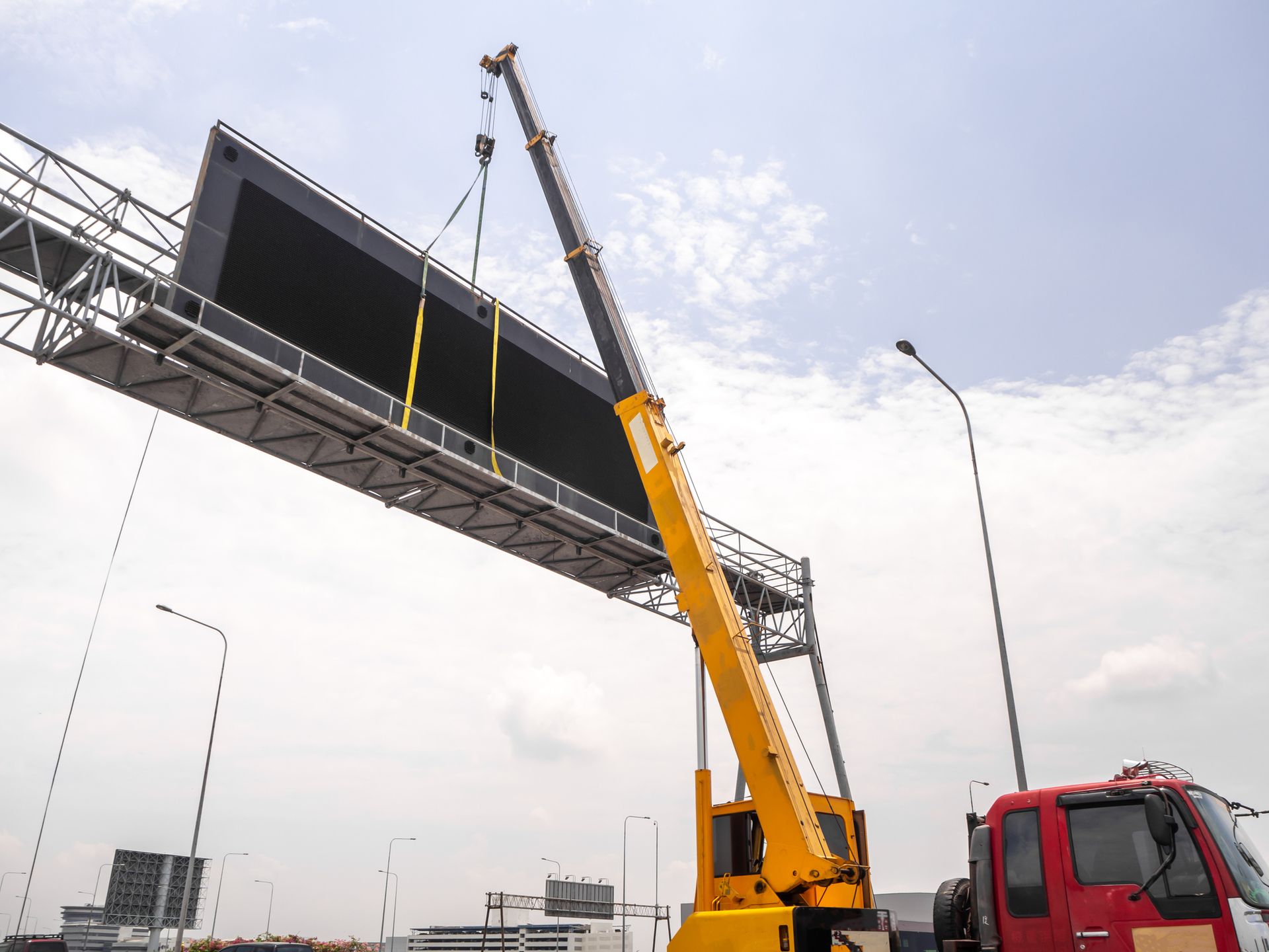 Crane rental lifting LED signboard at construction site with clear blue sky background.