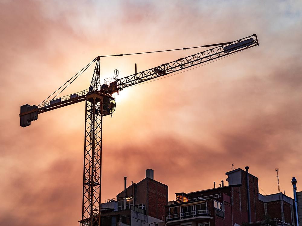 Construction crane silhouetted against a sunset sky, positioned above a building.