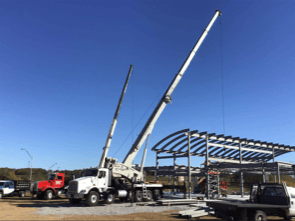 Cranes erecting steel framework of a building on a construction site under a blue sky.
